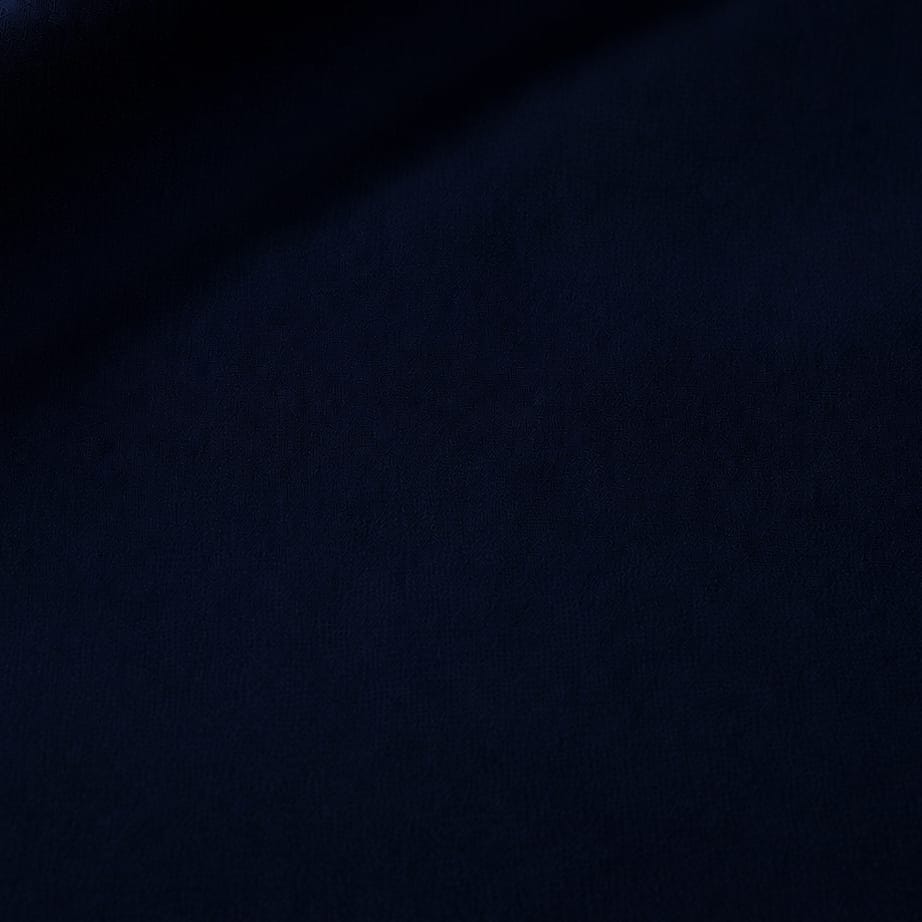 A close-up of dark navy blue fabric with a soft, textured surface and gentle folds.