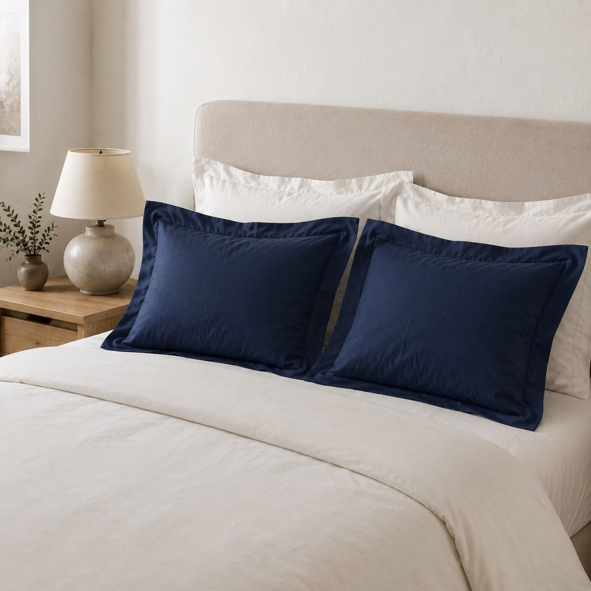Beddley Navy Blue cotton sateen pillow shams styled with white bedding in a bright neutral bedroom.